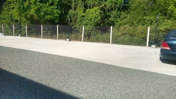 A parking area with a concrete surface, a chain-link fence, and a car parked on the right.