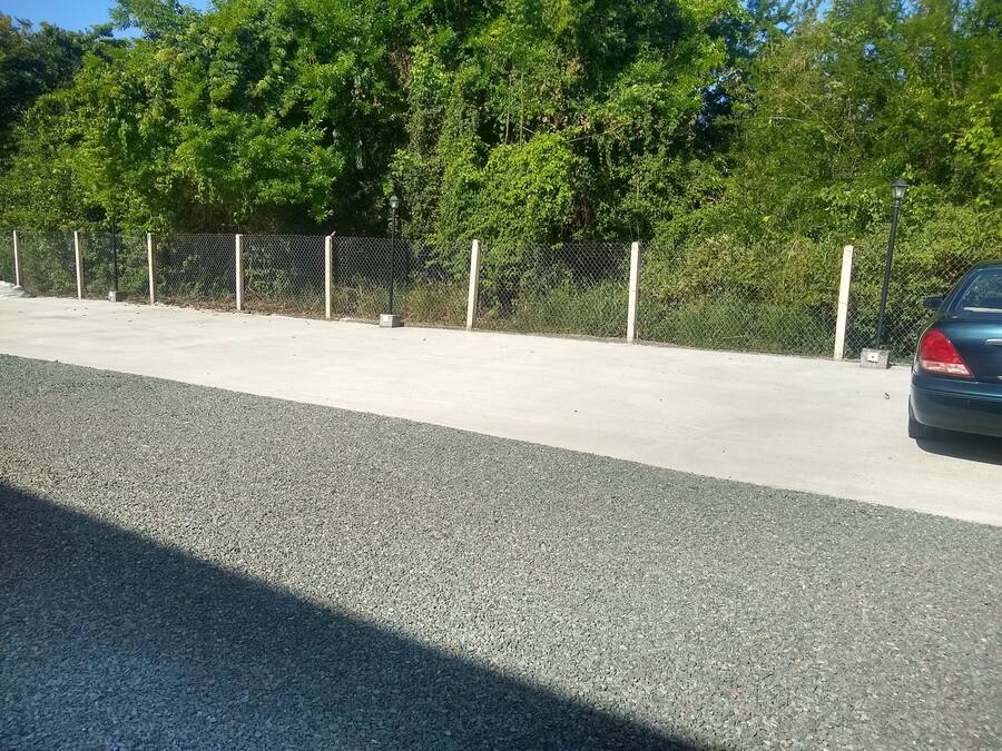 Un espace de stationnement avec une surface en béton, une clôture en treillis métallique et une voiture garée sur le côté droit.