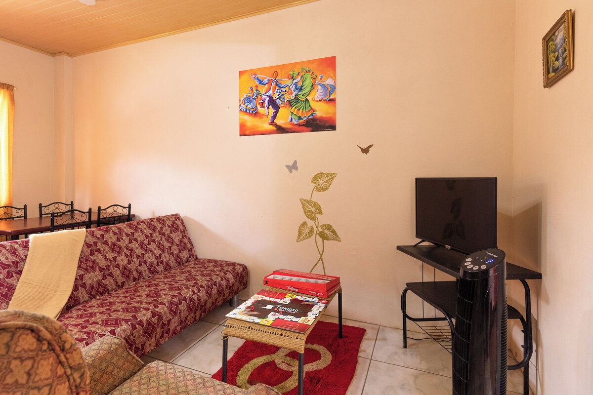 A living room with a sofa, a table with a board game, a TV, and a painting on the wall.