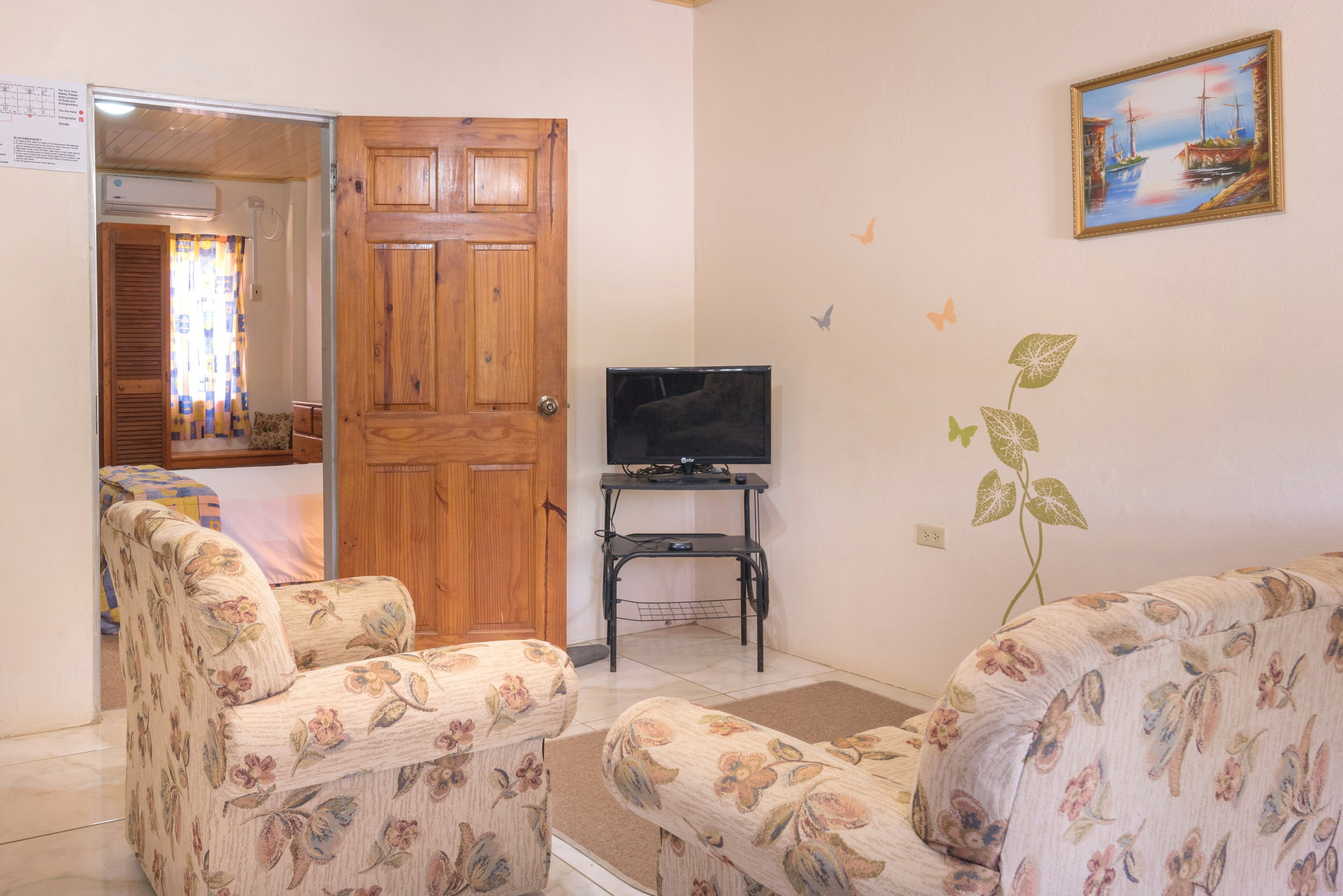 Ein Wohnzimmer mit floral gemusterten Sofas, einer Holztür, einem Fernseher auf einem Schrank und einem Gemälde an der Wand.