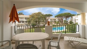 Un balcón con mesa y sillas, vista a una piscina y un complejo de edificios al fondo.