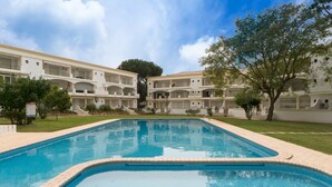 Una piscina rodeada por un edificio con varios balcones y un árbol.