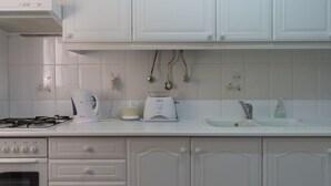 Una cocina con armarios blancos, estufa a gas, cafetera, licuadora y un lavamanos.