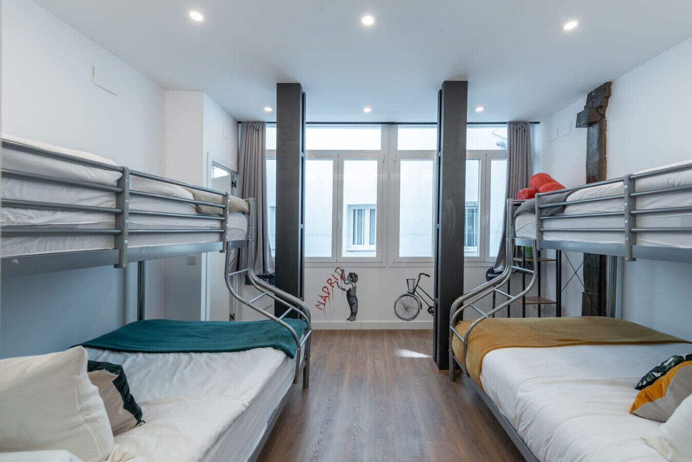 A dormitory room with bunk beds, a bicycle, and a mural on the wall.