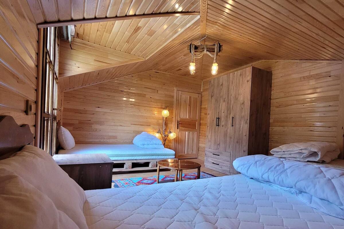 A cozy cabin-style room with a loft bed, a small table, and a wooden wardrobe.