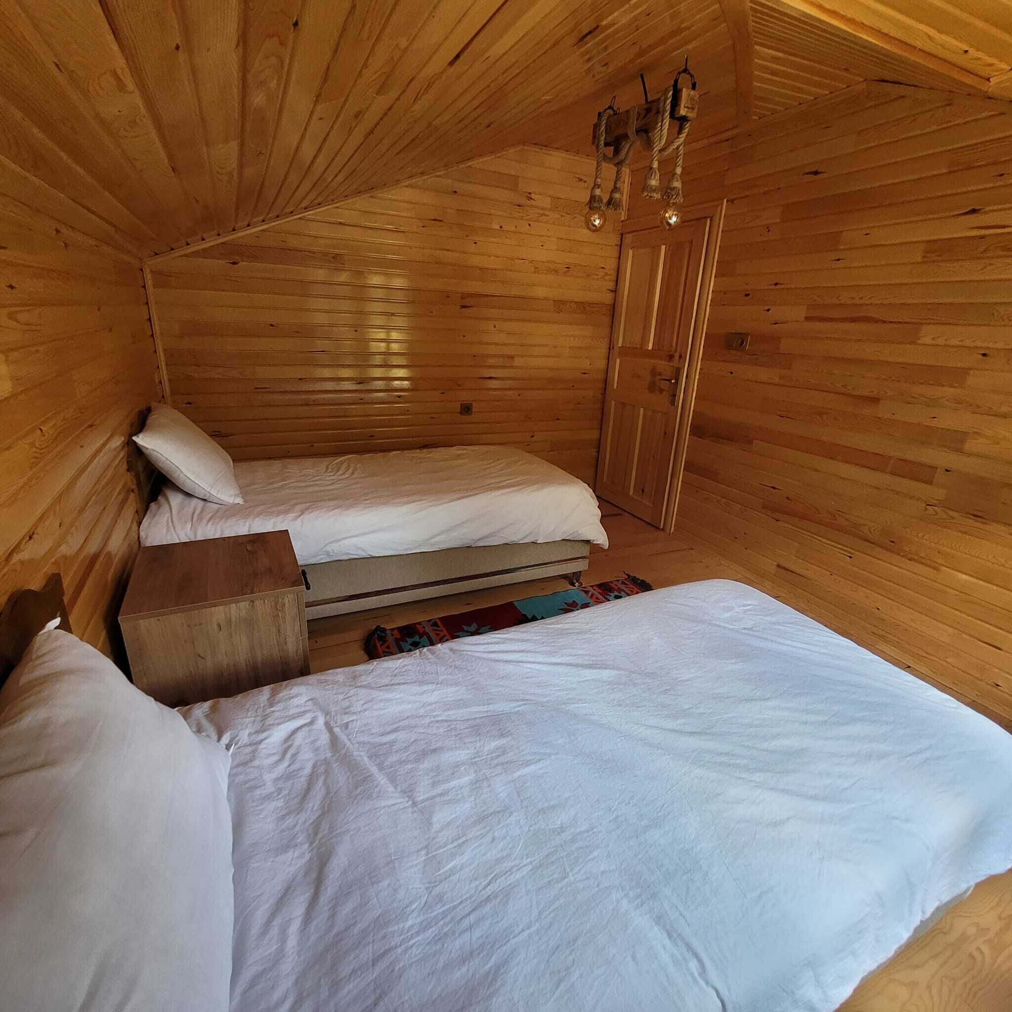 A cozy wooden cabin room with two beds, a wooden bench, and a door.