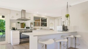 A modern kitchen with a central island, bar stools, stainless steel appliances, and a hanging plant.