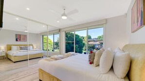 A modern bedroom with a large bed, a ceiling fan, and large windows offering a view of the outdoors.