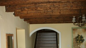 Una escalera con barandilla de madera que lleva a un piso superior, un armario de madera, una silla y una planta en maceta.
