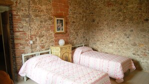 Una habitación con dos camas, una mesita de noche de madera, un cuadro en la pared y una pared de piedra.