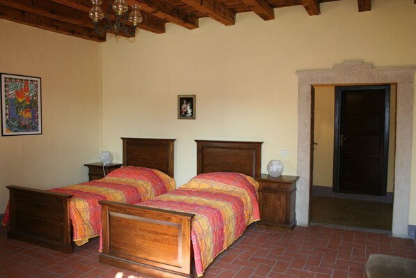 A bedroom with two wooden beds, a nightstand with a lamp, a framed picture on the wall, and a door leading to another room. - Lindoro - tasteful apt., garden, quiet, close to Peschiera del Garda (Veneto)