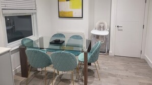 A modern dining area with a glass table and teal chairs, a white radiator, and a door with a white frame.