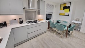 A modern kitchen with a central island, stainless steel appliances, and a dining area with teal chairs.