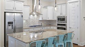 A modern kitchen with white cabinetry, a granite countertop, stainless steel appliances, and a central island with bar stools.