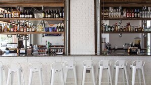 A bar with white brick walls, shelves stocked with various liquor bottles, and white metal bar stools.