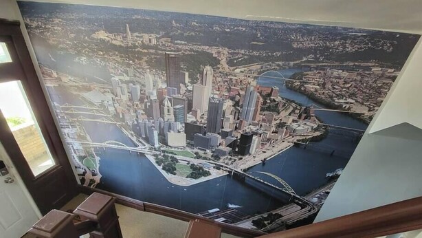 Ein großes Stadtbild-Mural an einer Treppenwand, das einen Fluss, Brücken und Wolkenkratzer zeigt.