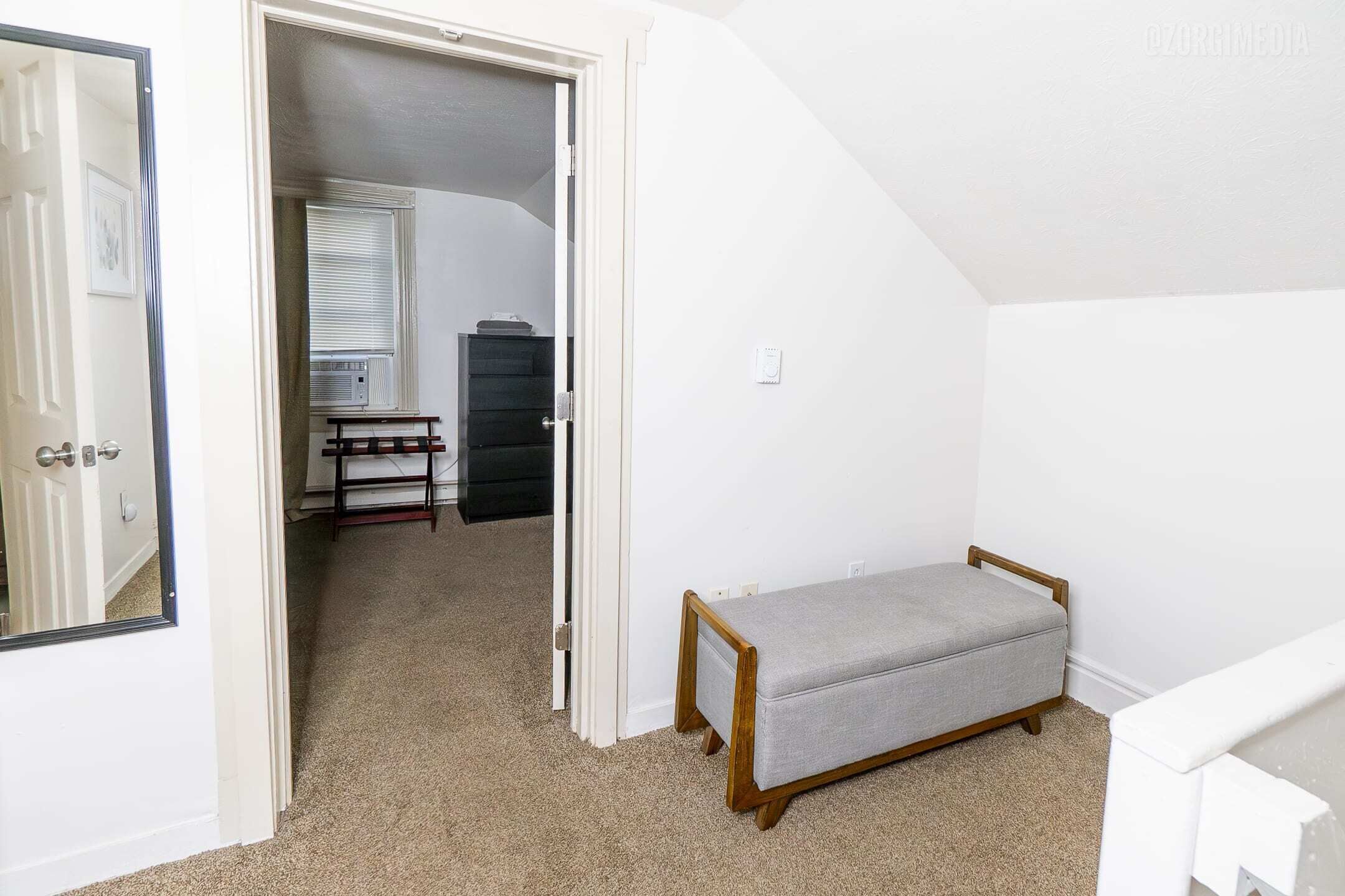 Een kamer met een bank, een deur en een gang die leidt naar een kamer met een radiator en een bureau.
