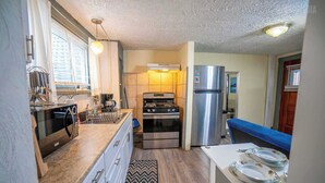 Une cuisine compacte équipée d’une cuisinière, d’un four et d’un réfrigérateur. On y trouve une table à manger avec des assiettes et un banc.