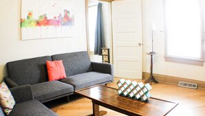 Una sala de estar con un sofá gris, una mesa de centro de madera y un cuadro abstracto y colorido en la pared.