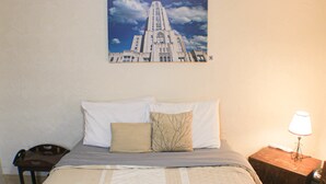 Una cama bien hecha con una colcha estampada, un cojín con diseño de rama de árbol y un cuadro en la pared de un edificio.