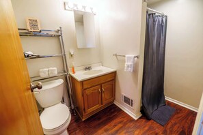 A bathroom with a white toilet, wooden vanity, and a shower curtain. - Carey Way Quarters - Explorer's Dream Pad (Pittsburgh)