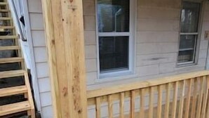 Une terrasse en bois avec une rambarde, une fenêtre et une porte.