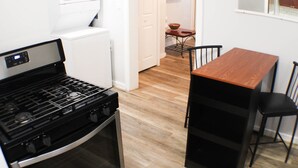 Une cuisine compacte équipée d’une cuisinière, d’un four et d’un réfrigérateur blanc. On y trouve une table à manger avec des chaises, ainsi qu’un petit coin repas avec une table et des chaises.