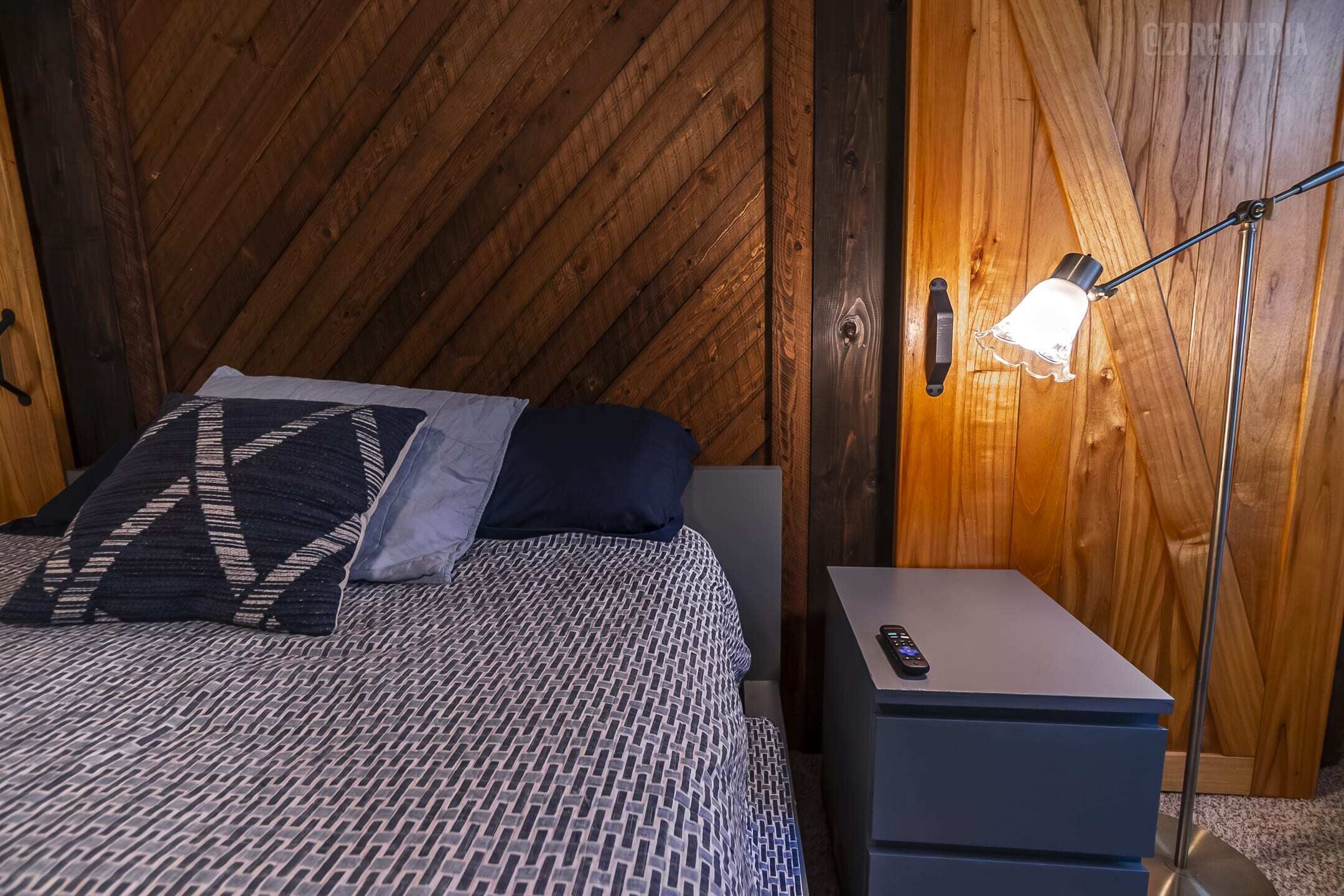 Un lit bien fait, avec une literie à motifs, une table de chevet avec une lampe et un mur en bois.