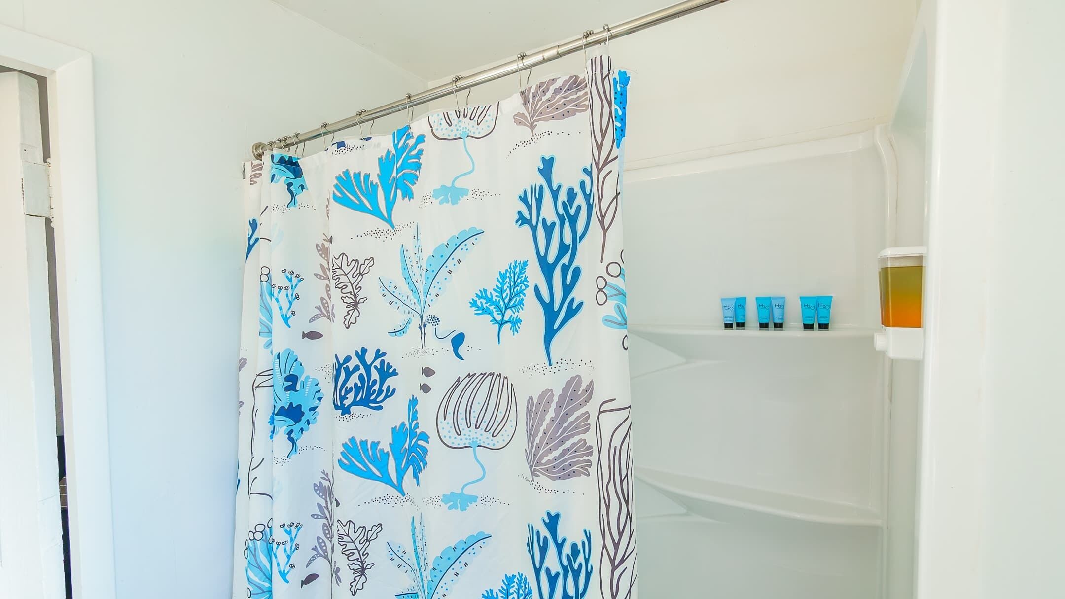 Ein Badezimmer mit Duschvorhang, der marine Muster in Blau und Weiß zeigt, einer weißen Badewanne und einem Regal mit vier blauen Flaschen.