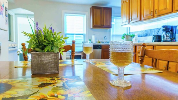 Une cuisine avec des meubles en bois, une table à manger recouverte d’une nappe à motifs floraux et un verre de vin.