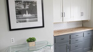 Een keuken met witte kastjes, een glazen tafel en een zwart-wit foto in een lijst aan de muur.