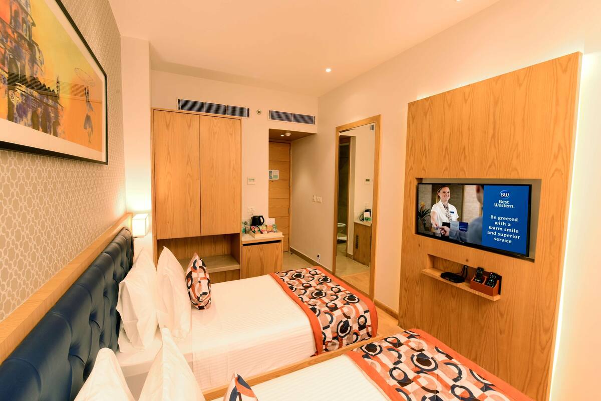 Een hotelkamer met twee bedden, een televisie, een houten garderobe en een schilderij aan de muur.