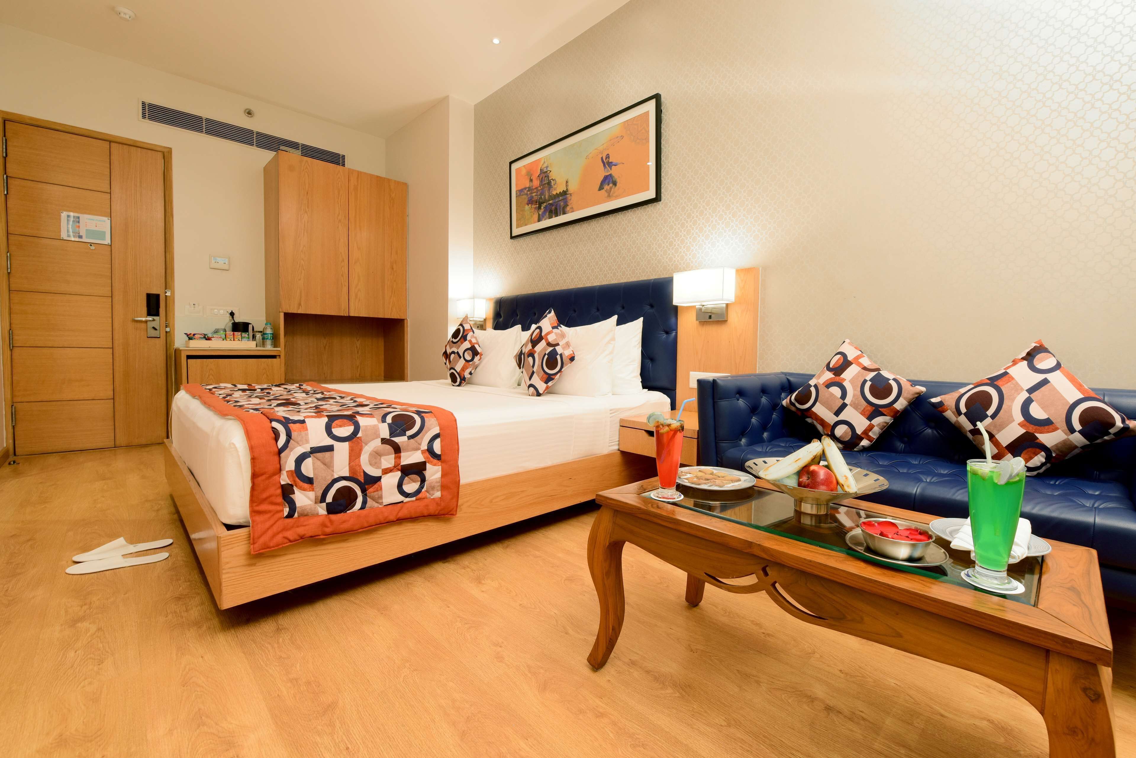 Hotelkamer met een bed, een bank, een bijzettafeltje met ontbijtartikelen en een schilderij aan de muur.