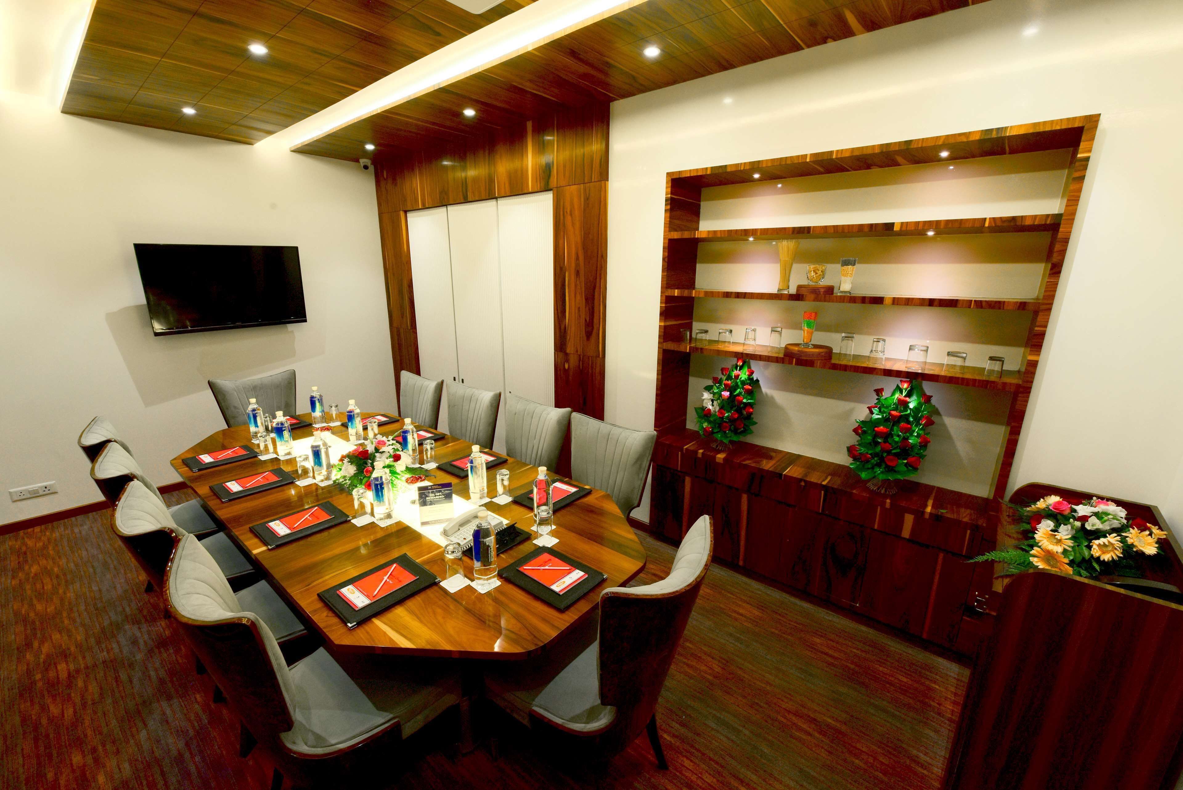 A conference room with a long wooden table, chairs, a TV mounted on the wall, and a decorative shelf with items.