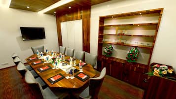 A conference room with a long wooden table, chairs, a TV mounted on the wall, and a decorative shelf with items.