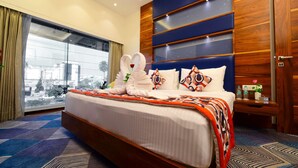 Een hotelkamer met een groot bed, een nachtkastje, een raam met uitzicht op de stad en een houten hoofdeinde.