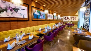 Een restaurant met houten lambrisering, een lange gele bank, paarse stoelen en meerdere kroonluchters.