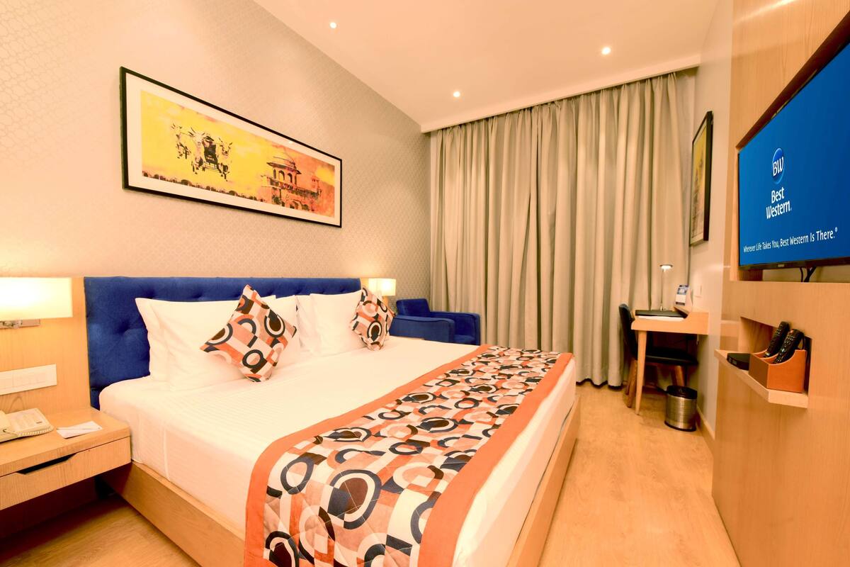 Een hotelkamer met een bed, een bureau, een stoel, een televisie en een schilderij aan de muur.