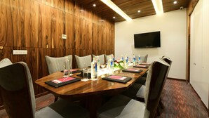 Een vergaderruimte met een houten paneelwand, een flatscreen televisie en een lange tafel met stoelen.