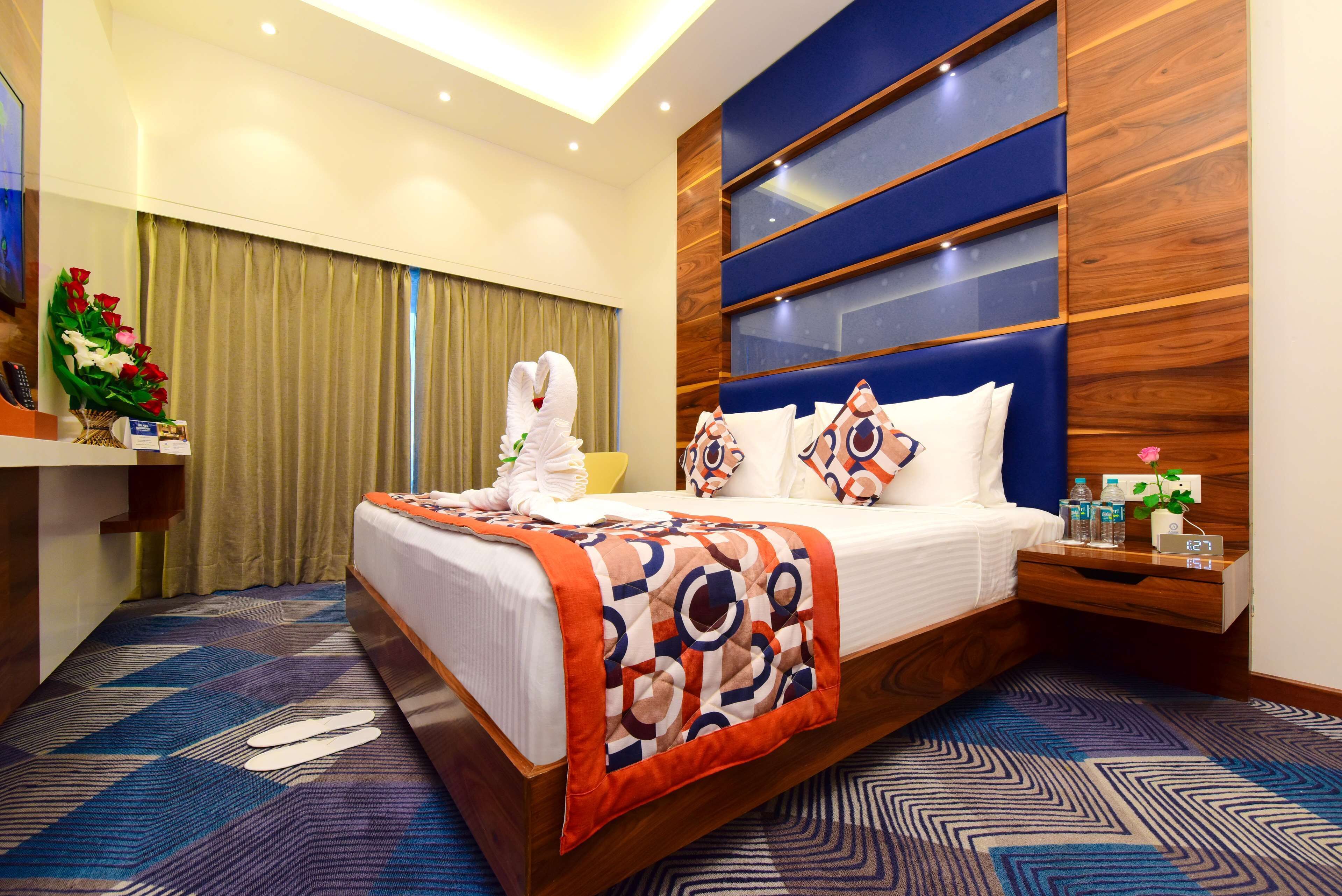 A hotel room with a large bed, a wooden headboard, a nightstand with a clock, and a desk with a telephone.