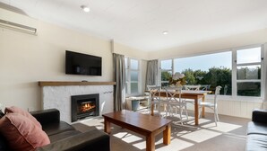 A living room with a fireplace, a television mounted on the wall, and a dining area with a table and chairs. - Townside Treat - Wanaka Holiday Home (Wanaka)