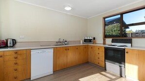 A modern kitchen with wooden cabinets, a white dishwasher, a microwave, and a built-in oven. - Downtown Delight - Wanaka Holiday Home (Wanaka)