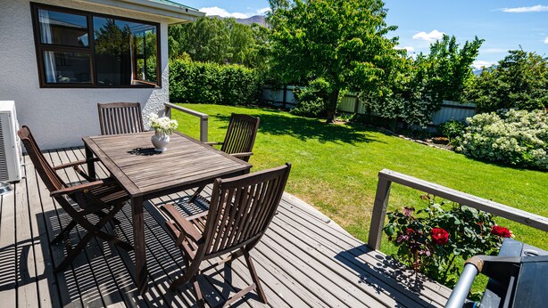 A wooden deck with a table and chairs, a potted plant, and a barbecue grill. - Downtown Delight - Wanaka Holiday Home (Wanaka)