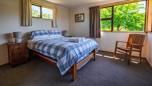 A bedroom with a bed, a chair, a nightstand, and a window with curtains. - Downtown Delight - Wanaka Holiday Home (Wanaka)