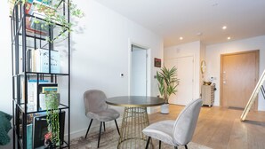 A modern living room with a round table, two grey chairs, a bookshelf, and a potted plant. - Urban Oasis | 1Bed | Pvt Balcony | Westbourne Park (London)