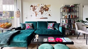 A modern living room with a teal sofa, a world map wall art, a bookshelf, and a dining area with a table and chairs. - Urban Oasis | 1Bed | Pvt Balcony | Westbourne Park (London)