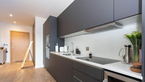 A modern kitchen with dark cabinets, a white countertop, and stainless steel appliances. - Urban Oasis | 1Bed | Pvt Balcony | Westbourne Park (London)