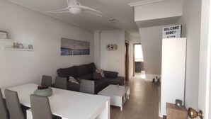 A modern living room with a white sofa, a dining table with chairs, a ceiling fan, and a 'Welcome Home' sign on the door. - Villa Terreros 365 days of sunshine (Pulpí)