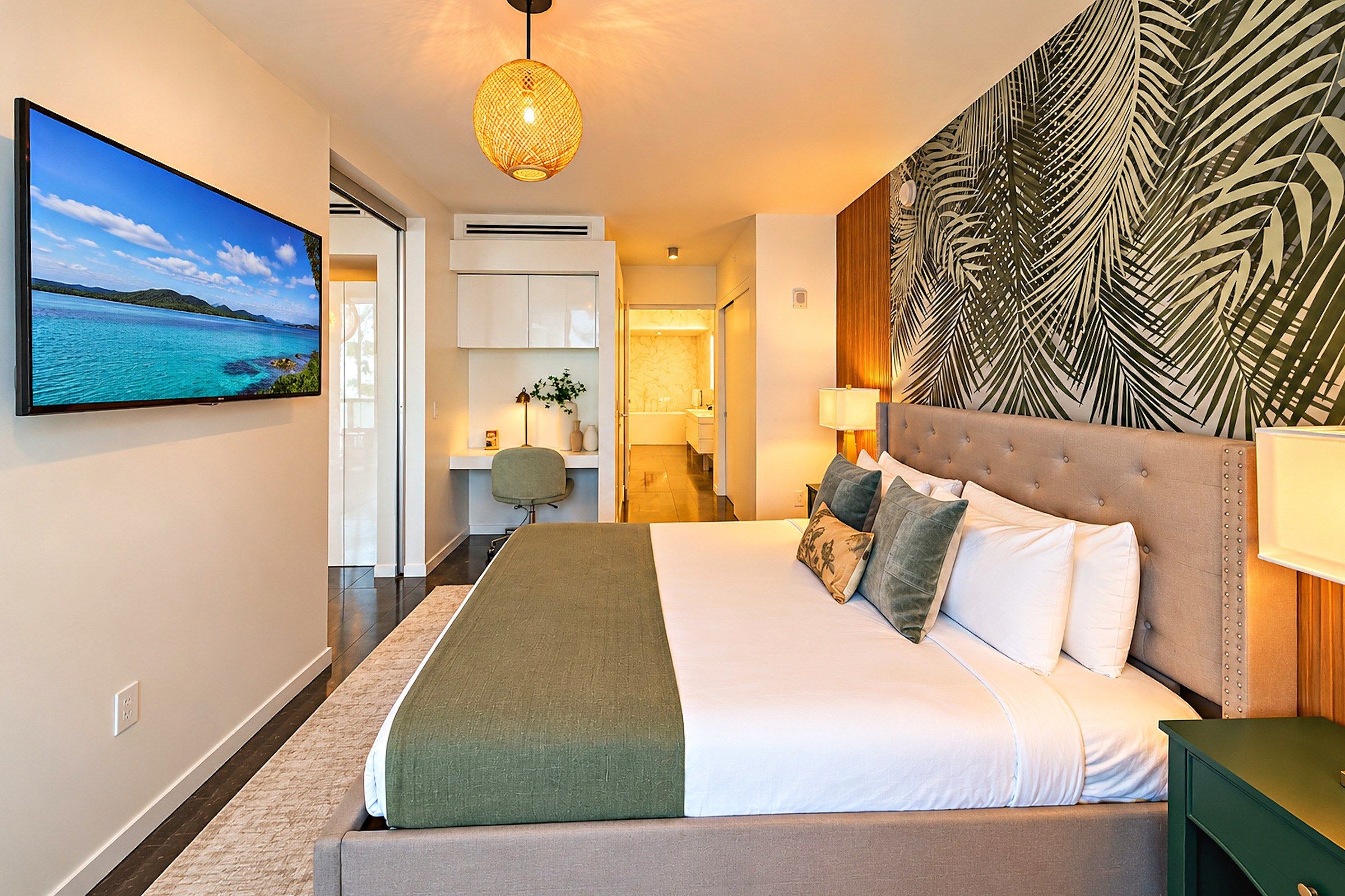 Une chambre d’hôtel dotée d’un grand lit, d’un téléviseur diffusant des images de paysages, d’un bureau avec une chaise et d’un panneau décoratif mural.