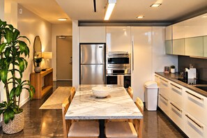 A modern kitchen with a marble countertop, stainless steel appliances, and a dining area with a wooden table and chairs. - Luxury Suite w/ Rooftop Pool • Beach Steps Away (Miami Beach)